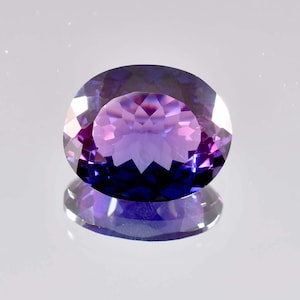 Può includere: Una grande gemma di ametista di forma ovale con un gradiente di colore viola e blu. La gemma è sfaccettata e ha un'alta lucidatura.