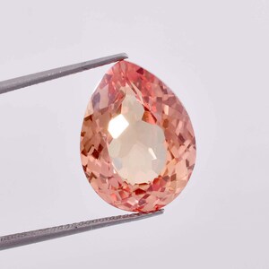 May include: A pear-shaped gemstone with a peach and orange color gradient. The gemstone is faceted and has a high polish.