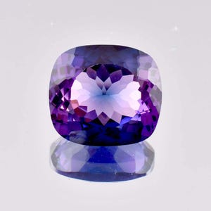 以下が含まれることがあります： クッションカットの紫水晶で、紫色と青色のグラデーションになっています。宝石はファセットカットされており、高い光沢があります。
