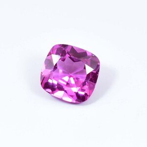 Puede incluir: Una gema rosa vibrante con un corte cojín. La gema está facetada y tiene un alto nivel de brillo.