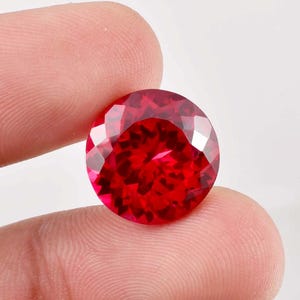 May include: A deep red round gemstone with a faceted cut.