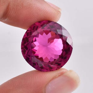 Può includere: Una pietra preziosa rotonda e sfaccettata di colore rosa. La pietra preziosa presenta un motivo a forma di stella al centro.