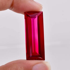 May include: A deep red rectangular gemstone with a faceted cut.