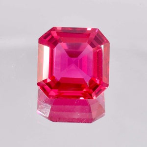May include: A vibrant pink gemstone with a square emerald cut. The gemstone is faceted and has a high polish.