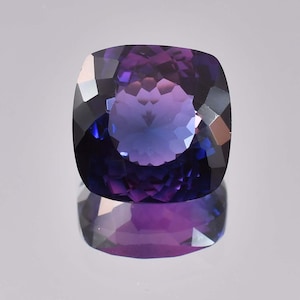 Può includere: Una pietra preziosa a taglio cuscino con un gradiente di colore dal viola scuro al blu. La gemma è sfaccettata e ha un'alta lucidatura.