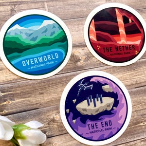 May include: Three round stickers with colorful illustrations and text. The first sticker is blue and green with the text "Overworld - National Park -." The second sticker is red and orange with the text "The Nether - National Park -." The third sticker is purple and blue with the text "The End - National Park -."