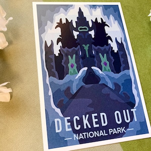 Puede incluir: Una postal con una ilustración azul y morada de un castillo con el texto "DECKED OUT - NATIONAL PARK" en la parte inferior.