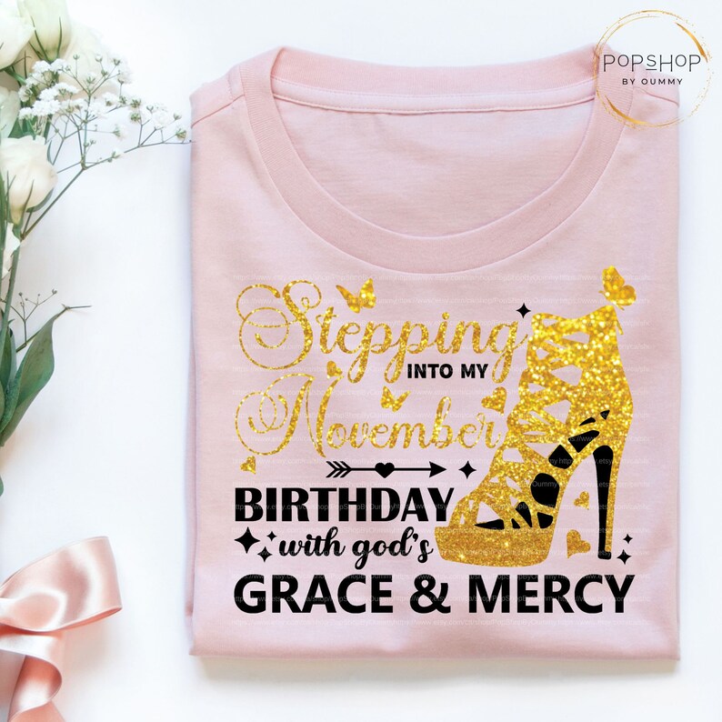 May include: Pink t-shirt with a gold glitter high heel shoe and the text "Stepping into my November Birthday with God's Grace & Mercy".