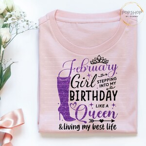 May include: Pink t-shirt with a purple glitter design that says "February Girl Stepping into my Birthday Like a Queen & living my best life".