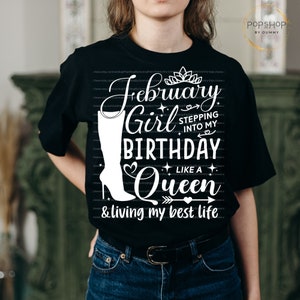 May include: Black t-shirt with white text that reads "February Girl Stepping into my Birthday Like a Queen & living my best life". The text is surrounded by hearts, stars, and a crown.