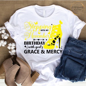 May include: White t-shirt with black text that reads "Stepping into my November Birthday with god's GRACE & MERCY". A yellow high-heeled shoe with a butterfly on the side is in the text.