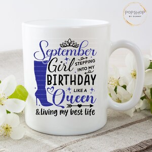 K&ouml;nnte beinhalten: Wei&szlig;e Keramiktasse mit einem blauen und schwarzen Design, auf dem "September Girl Stepping into My Birthday Like a Queen & Living My Best Life" steht.