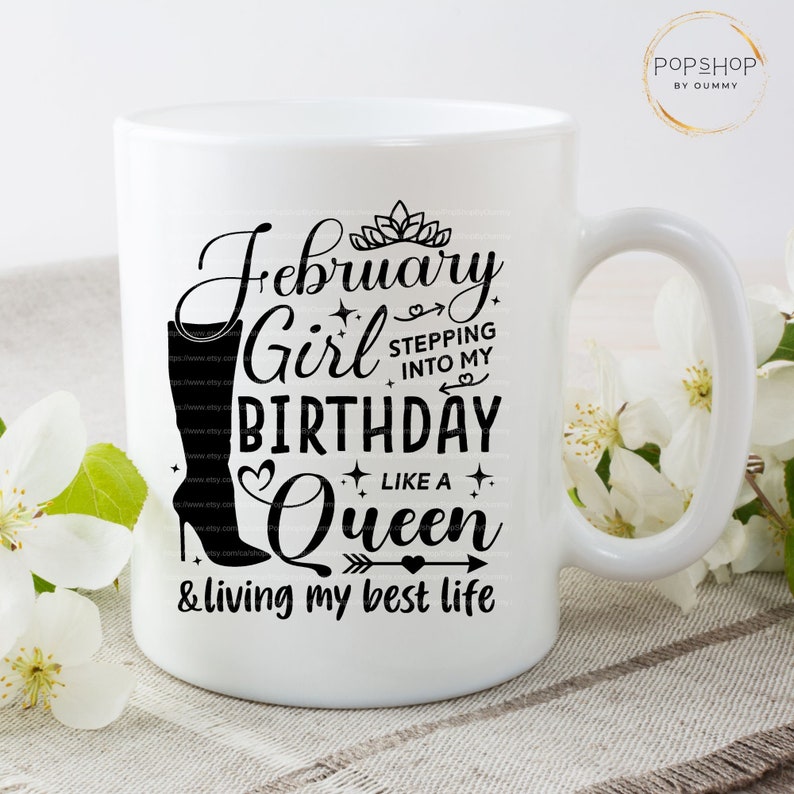 May include: White ceramic mug with a black design that says "February Girl Birthday Like a Queen & living my best life". The design also includes a crown, a heart, an arrow, and a boot.