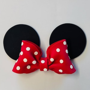 Puede incluir: Lazo rojo con lunares blancos y dos círculos de fieltro negro, que se asemejan a las orejas de Mickey Mouse.