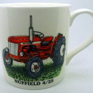 May include: White ceramic mug with a red Nuffield 4/25 tractor design. The tractor has a silver grill, black tyres, and is set on a green grassy base. The mug has a curved handle and the text "NUFFIELD 4/25" is printed at the bottom.