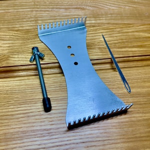 May include: A set of metal tools, including a comb-like piece, a needle, and a threaded rod with a wing nut. The tools are silver and lie on a wooden surface. The comb-like tool has a series of teeth along its edges.