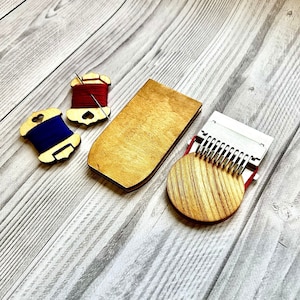 May include: A wooden embroidery hoop with a metal tensioning mechanism, two wooden thread bobbins with red and blue thread, and a wooden storage box.