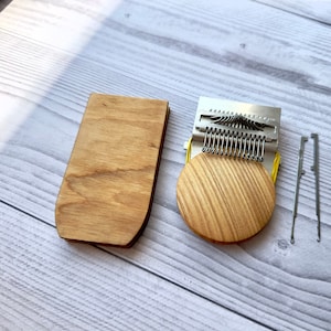 Peut inclure: Un ensemble d'outils de tissage en bois, comprenant une pièce rectangulaire en bois, une pièce ronde en bois avec des dents métalliques et deux outils métalliques. Les articles sont disposés sur une surface en bois clair.