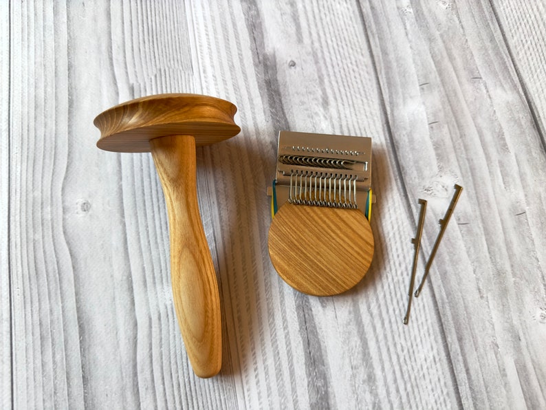 Puede incluir: Un torno de madera para hilados con una base redonda y un mango. Junto a &eacute;l hay un telar de punto de metal con una base de madera y dos agujas de tejer.