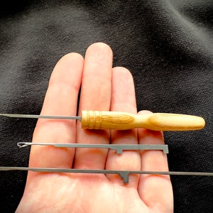 May include: Three metal crochet hooks with wooden handles. The hooks are different sizes and are held in a hand.