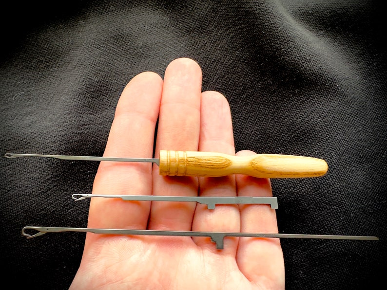 May include: Three metal crochet hooks with wooden handles. The hooks are different sizes and are held in a hand.