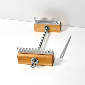 May include: A weaving loom tool consisting of two rectangular wooden blocks, each topped with a silver metal comb featuring numerous teeth. The blocks are connected by a central silver metal rod with wing nuts at each end, accompanied by a needle.