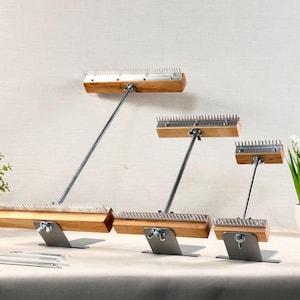 May include: Three wooden weaving combs with metal teeth, each mounted on a gray metal stand with a wing nut adjustment. The combs are arranged in descending size order, featuring light brown wood blocks and silver-colored metal rods and teeth.