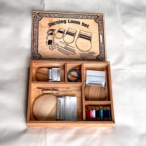 May include: A wooden darning loom set in a partitioned box with a hinged lid featuring the text Darning Loom Set by SPEEDWEVE. The kit includes three circular wooden looms with metal hooks, various metal needles, elastic bands, and colourful thread spools.