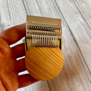 Puede incluir: Un primer plano de un telar de punto de madera circular con un accesorio de aguja de metal. El telar es circular y tiene un acabado de madera natural. El accesorio de aguja es plateado y tiene varias filas de peque&ntilde;os ganchos.