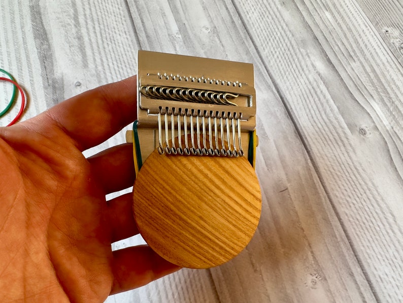 Puede incluir: Un primer plano de un telar de punto de madera circular con un accesorio de aguja de metal. El telar es circular y tiene un acabado de madera natural. El accesorio de aguja es plateado y tiene varias filas de peque&ntilde;os ganchos.