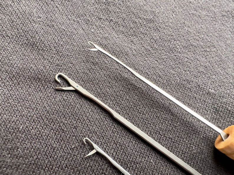 May include: Three silver crochet hooks of different sizes, with one hook having a wooden handle.