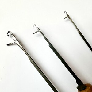 Pu&ograve; includere: Tre uncinetti in metallo con manici in legno. Gli uncinetti sono di dimensioni diverse e hanno una punta appuntita e un anello all'estremit&agrave;.