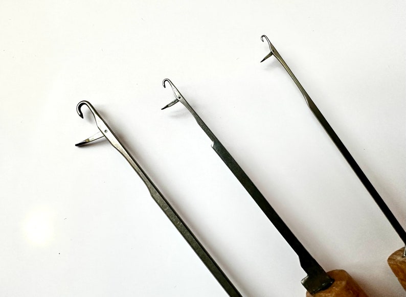Pu&ograve; includere: Tre uncinetti in metallo con manici in legno. Gli uncinetti sono di dimensioni diverse e hanno una punta appuntita e un anello all'estremit&agrave;.