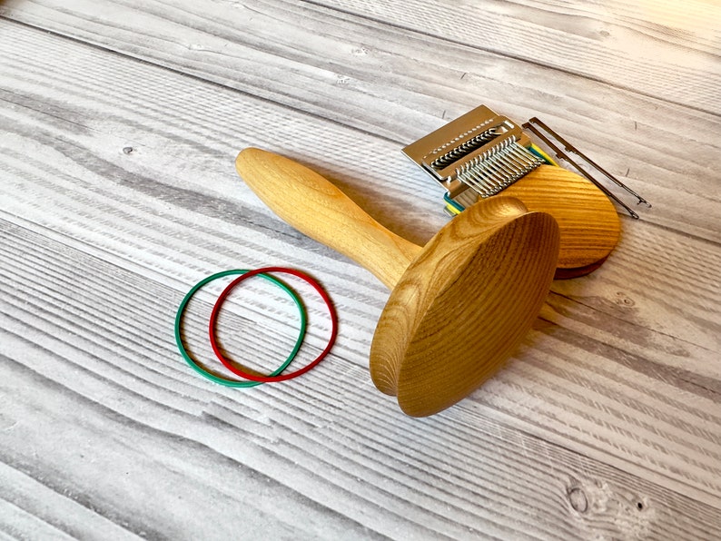 Puede incluir: Dos telares de punto de madera con mango, una aguja de tejer de metal y dos gomas el&aacute;sticas de color rojo y verde.