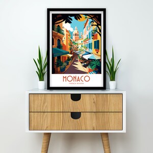 May include: A colorful illustration of a street scene in Monaco, France. The image features a narrow street lined with colorful buildings, palm trees, and people walking. The text "MONACO FRENCH RIVIERA" is printed at the bottom of the image.