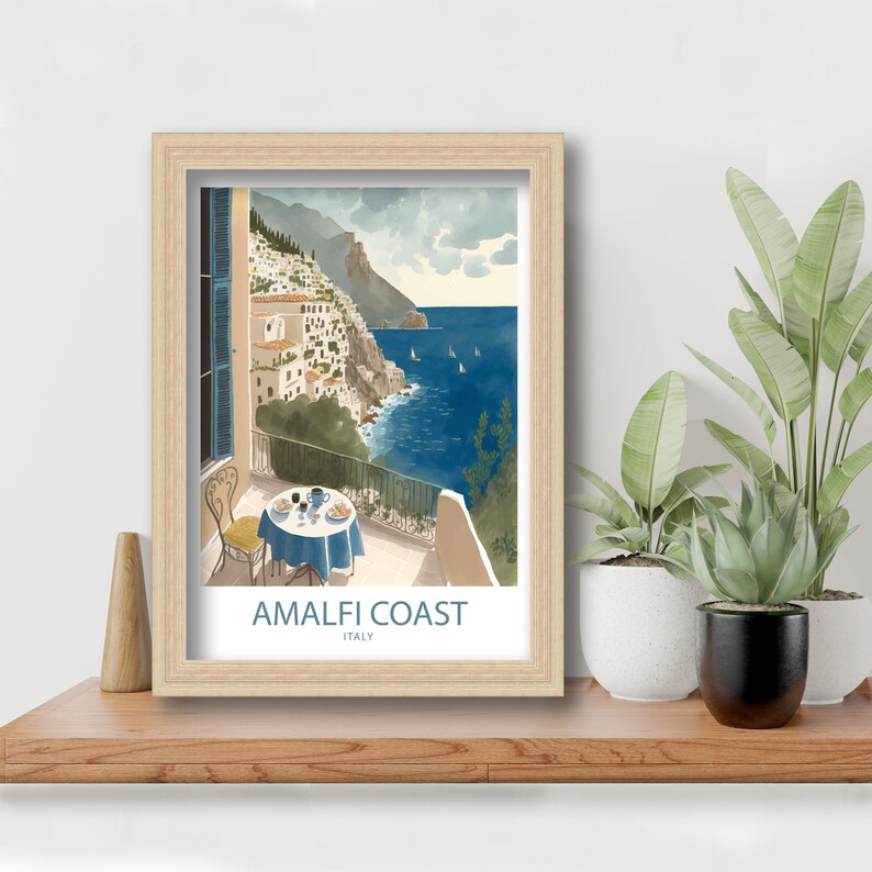 Może przedstawiać: Wydruk w ramie akwareli przedstawiający balkon z widokiem na wybrzeże Amalfi we Włoszech. Balkon ma st&oacute;ł z niebieskim obrusem i kieliszek wina. Widok pokazuje miasto zbudowane na klifach z morzem w tle. Wydruk zawiera tekst "Amalfi Coast, Italy" na dole.