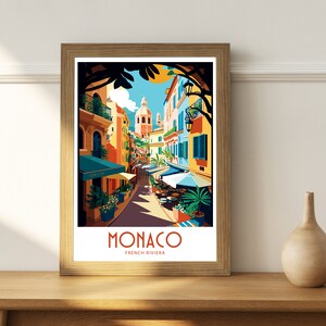 May include: A colorful illustration of a street scene in Monaco, French Riviera. The image features a narrow street lined with colorful buildings, palm trees, and outdoor cafes. The text "MONACO FRENCH RIVIERA" is displayed at the bottom of the image.