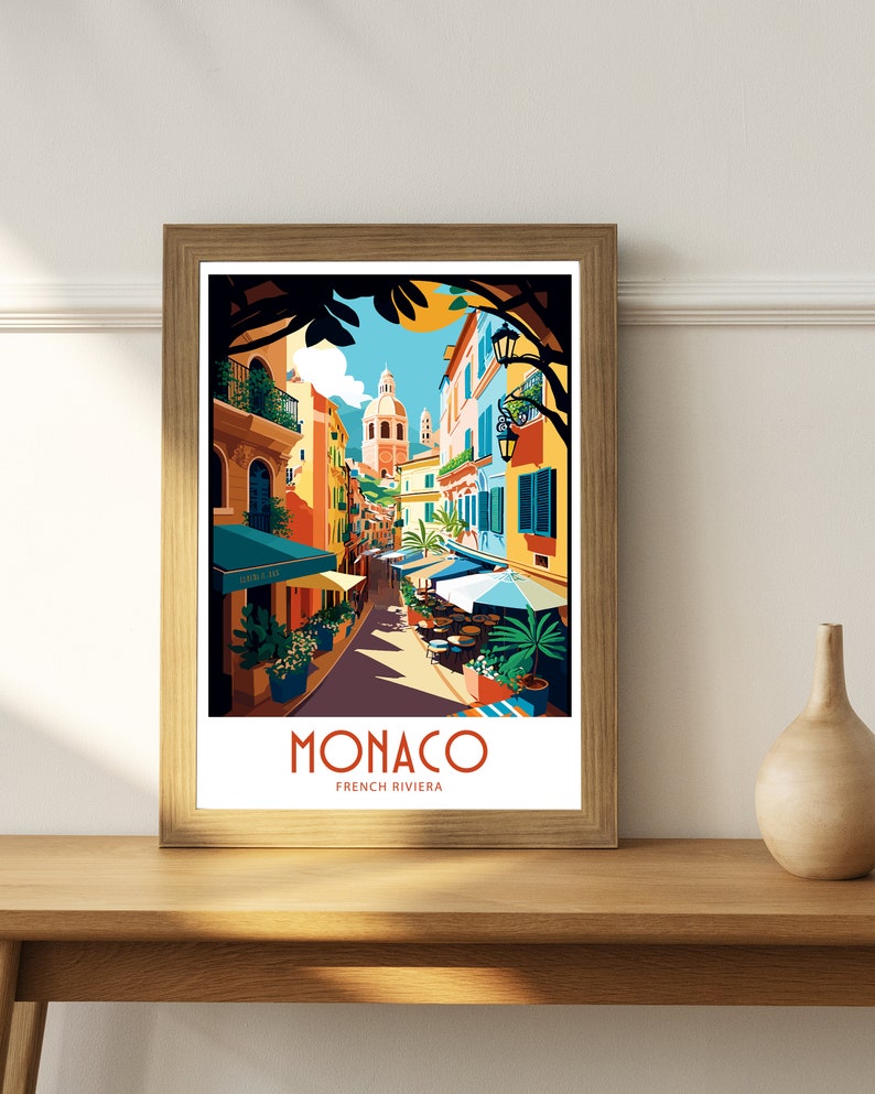 May include: A colorful illustration of a street scene in Monaco, French Riviera. The image features a narrow street lined with colorful buildings, palm trees, and outdoor cafes. The text "MONACO FRENCH RIVIERA" is displayed at the bottom of the image.