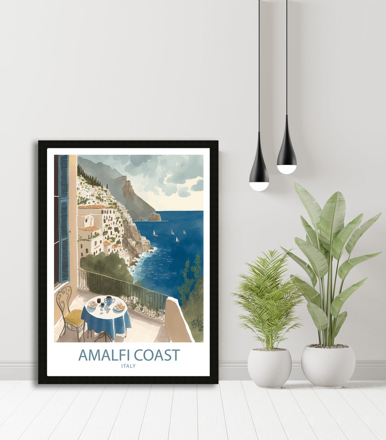 Może przedstawiać: Ilustracja w ramie przedstawiająca kolorową scenę na wybrzeżu Amalfi we Włoszech. Obraz przedstawia balkon z widokiem na ocean z stołem i krzesłami ustawionymi dla dw&oacute;ch os&oacute;b. Tekst "Amalfi Coast" i "Italy" jest wydrukowany pod obrazem.