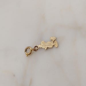 May include: A gold-coloured charm with a small clasp. The charm is in the shape of a stylized figure. The text "The Old Jewelry Chest" is visible in the image.