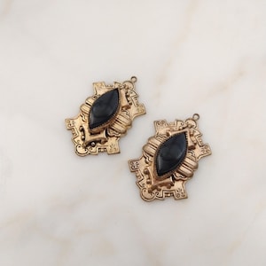 May include: Two antique gold-toned pendants with a black, oval-shaped stone center. The pendants have an ornate, filigree design around the stone and a small loop at the top for attaching to a chain or other jewelry component. The Old Jewelry Chest.