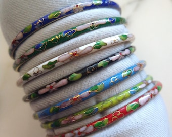 May include: A stack of eight thin metal bangles featuring cloisonné enamel work. Each bangle displays a floral pattern with pink petals and green leaves outlined in gold wire, set against various background colors including blue, green, white, black, light blue, yellow, and red.