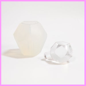 以下が含まれることがあります： 透明なファセットガラスボトルと、それに合うストッパー。ボトルは幾何学的なデザインで、つや消し加工が施されています。ストッパーは透明で、同様のファセット形状をしています。白い背景にあります。