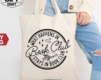 May include: A cream-colored tote bag with black text that reads "What happens in Book Club stays in Book Club." The bag has a circular design with a book and floral elements. The bag is held by a person wearing a cream-colored cardigan and blue jeans.