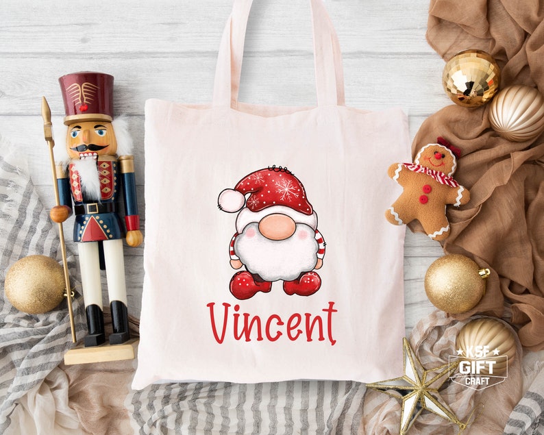 May include: A pink tote bag with a white gnome illustration wearing a red and white hat. The gnome is holding a red and white candy cane. The bag has the name "Vincent" printed in red letters.
