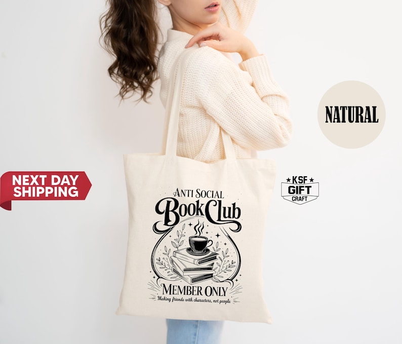 Op de afbeelding: Een cr&egrave;mekleurige draagtas met de tekst "ANTI SOCIAL Book Club" in een decoratief lettertype. Het ontwerp bevat een stapel boeken, een koffiekopje en de tekst "MEMBER ONLY". De tas is gemaakt van een natuurlijke stof.