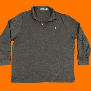 Könnte beinhalten: Ein dunkelgraues Langarm-Poloshirt mit braunem Kragen und kleinem gesticktem Logo auf der Brust. Das Shirt hat ein klassisches Design mit Knopfkragen und ist aus einem weichen, bequemen Material gefertigt.