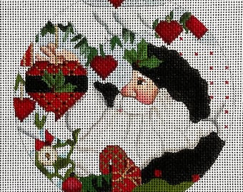 May include: A needlepoint Christmas ornament featuring a Santa Claus design. The ornament is circular, with a white background and a detailed depiction of Santa's face, a black beard, and red heart-shaped accents.
