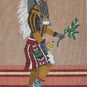 Op de afbeelding: Naaldkunst afbeelding van een Indiaanse figuur in traditionele kledij. De figuur staat in profiel, houdt een groene tak vast, met een hoofdtooi en kleding met patronen in bruin, rood, blauw en goud. De achtergrond heeft horizontale strepen.