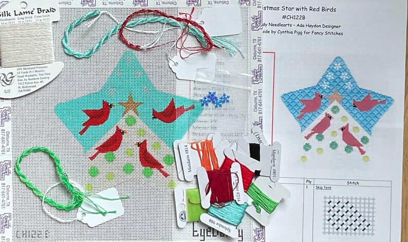 May include: Needlepoint canvas featuring a star design with red birds and a gold star. The canvas is accompanied by various threads, including green, red, and white, and a printed pattern guide. The text on the canvas reads "Christmas Star with Red Birds".